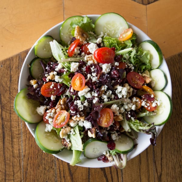 A vibrant salad with mixed greens, cherry tomatoes, cucumbers, feta cheese, walnuts, and dried cranberries.