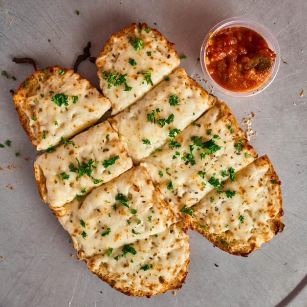 Cheesy garlic bread sticks with parsley and a side of marinara sauce on a metal surface.