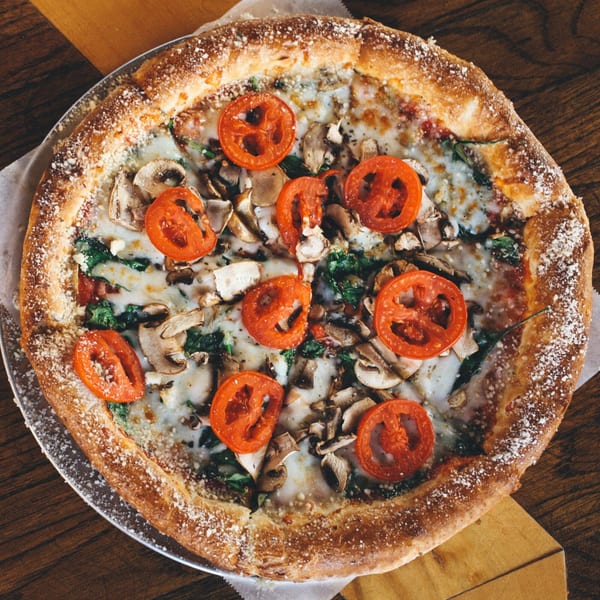 A DaVinci's Pizzeria pizza with tomatoes, mushrooms, spinach, and melted cheese on a wooden table.