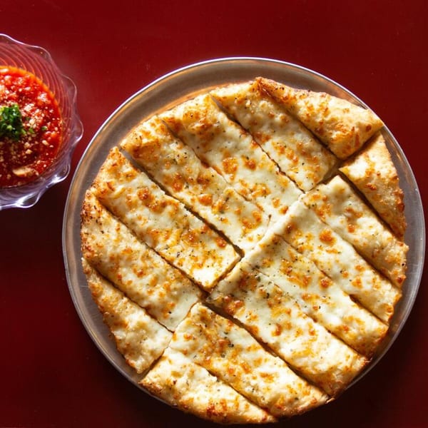 Cheesy garlic breadsticks on a metal tray with a side of marinara sauce.