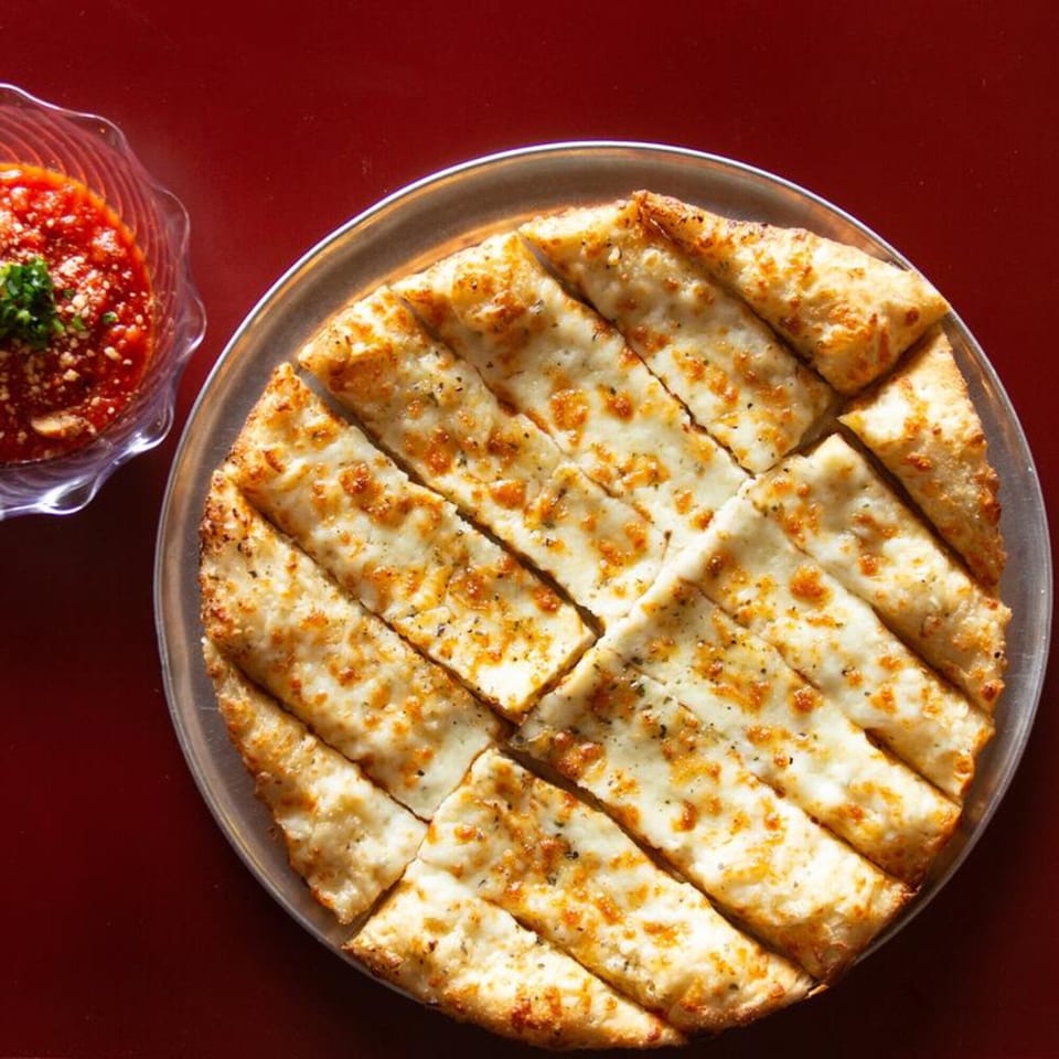 Cheesy garlic breadsticks on a metal tray with a side of marinara sauce.